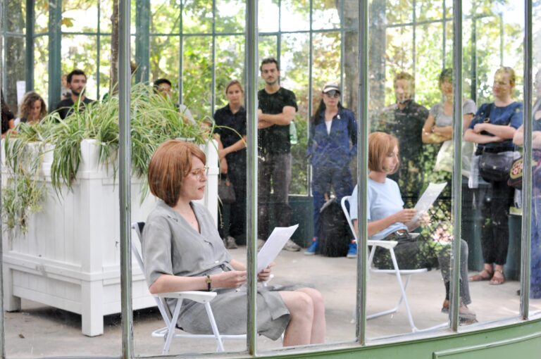 photo d'un performance dans une verrière de Charlotte et Clélia lisant un texte avec la même perruque